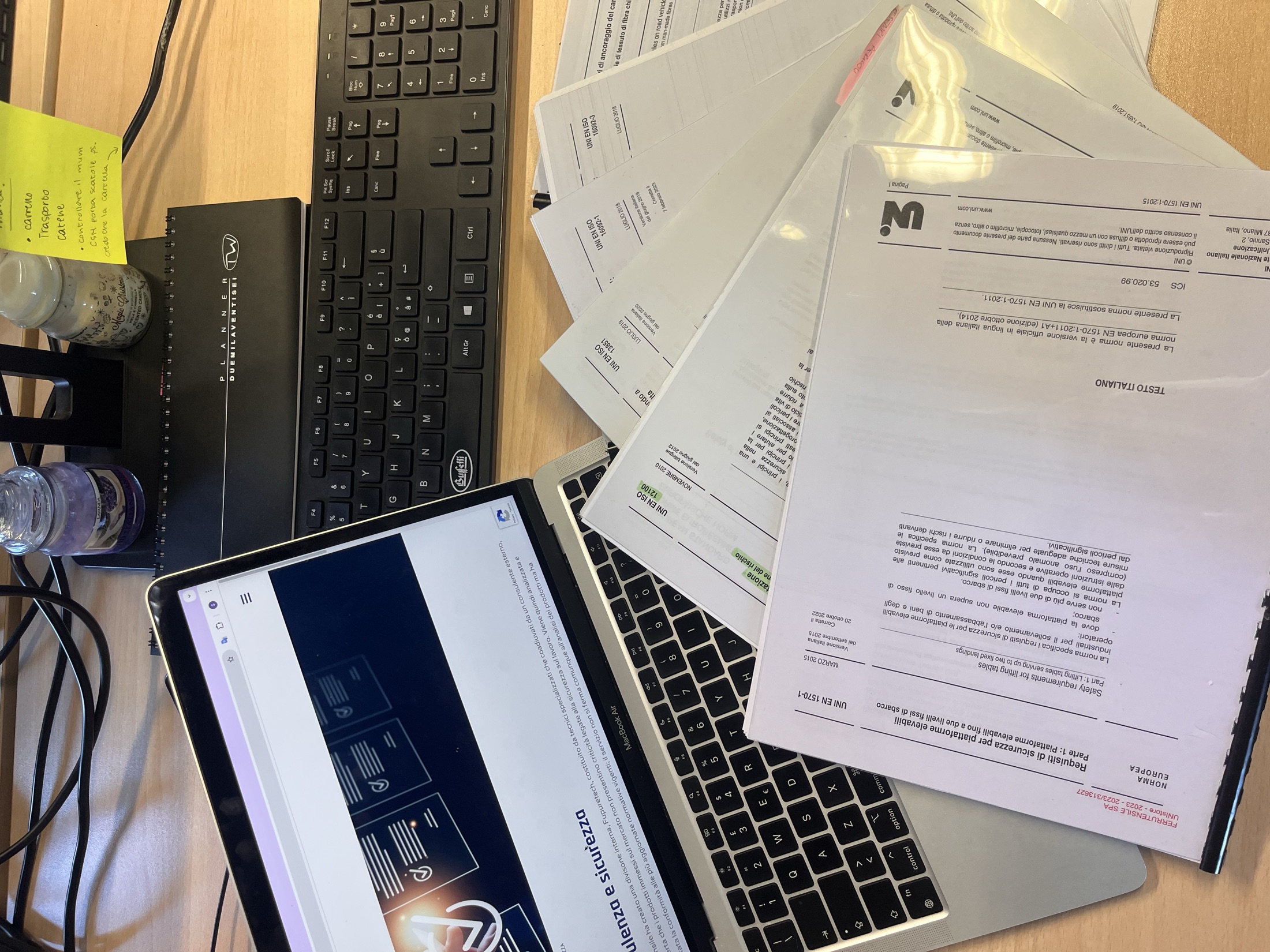 Norme UNI EN ISO aperte sulla scrivania, accanto al portatile con la pagina Consulenza e sicurezza
